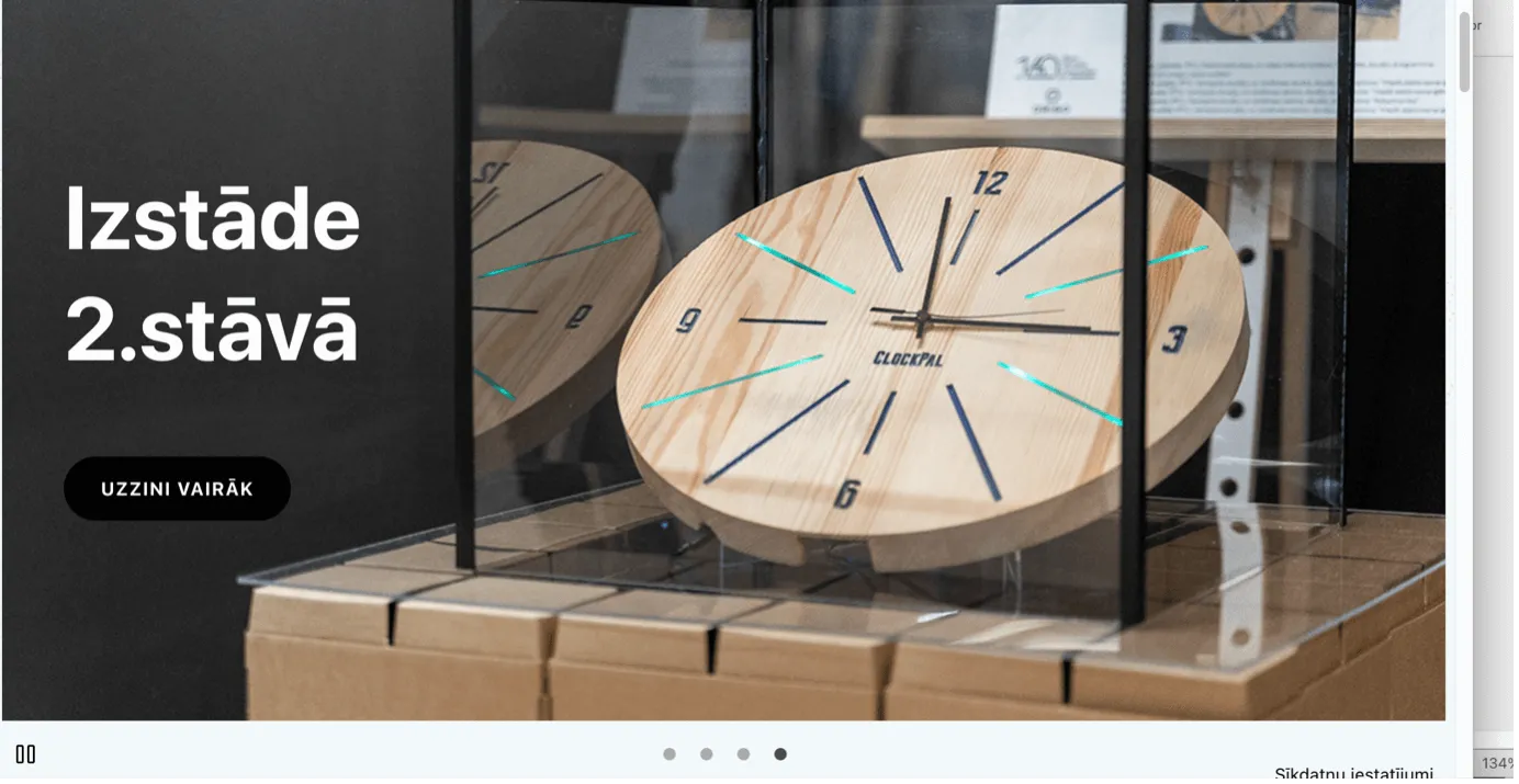 Kustīga attēla ekrānšāviņš no Latvijas tīmekļvietnes ar uzrakstu - Izstāde otrajā stāvā un koka sienas pulksteni fonā
